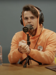 Gijs Niehe in oranje trui voor een microfoon