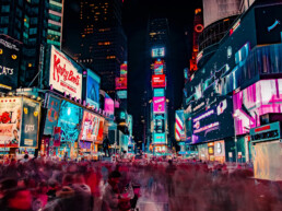 Een foto van Times Square in New York in het donker. We zien een mensenmassa en veel lichtgevende reclameborden.